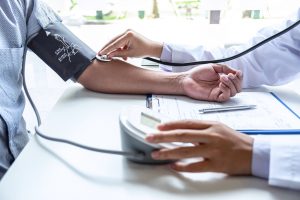 Doctor using stethoscope checking measuring arterial blood pressure on arm to a patient in the